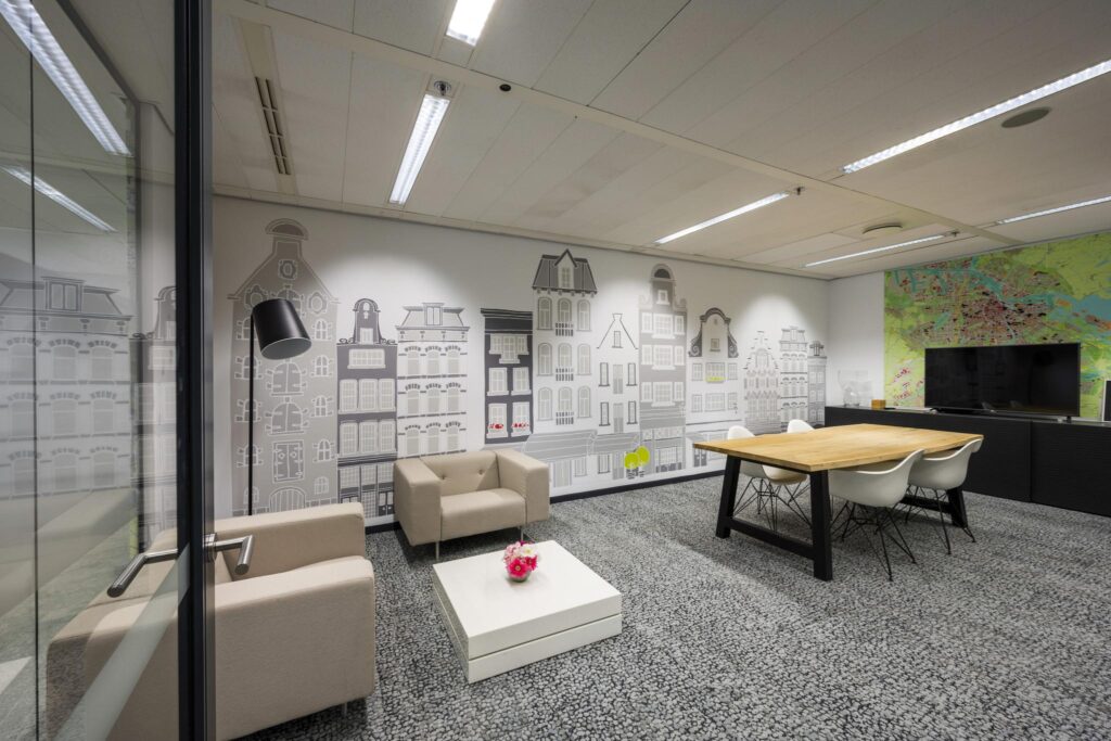 Modern meeting room with a wall mural of Amsterdam canal houses and a large map next to a flat-screen TV.